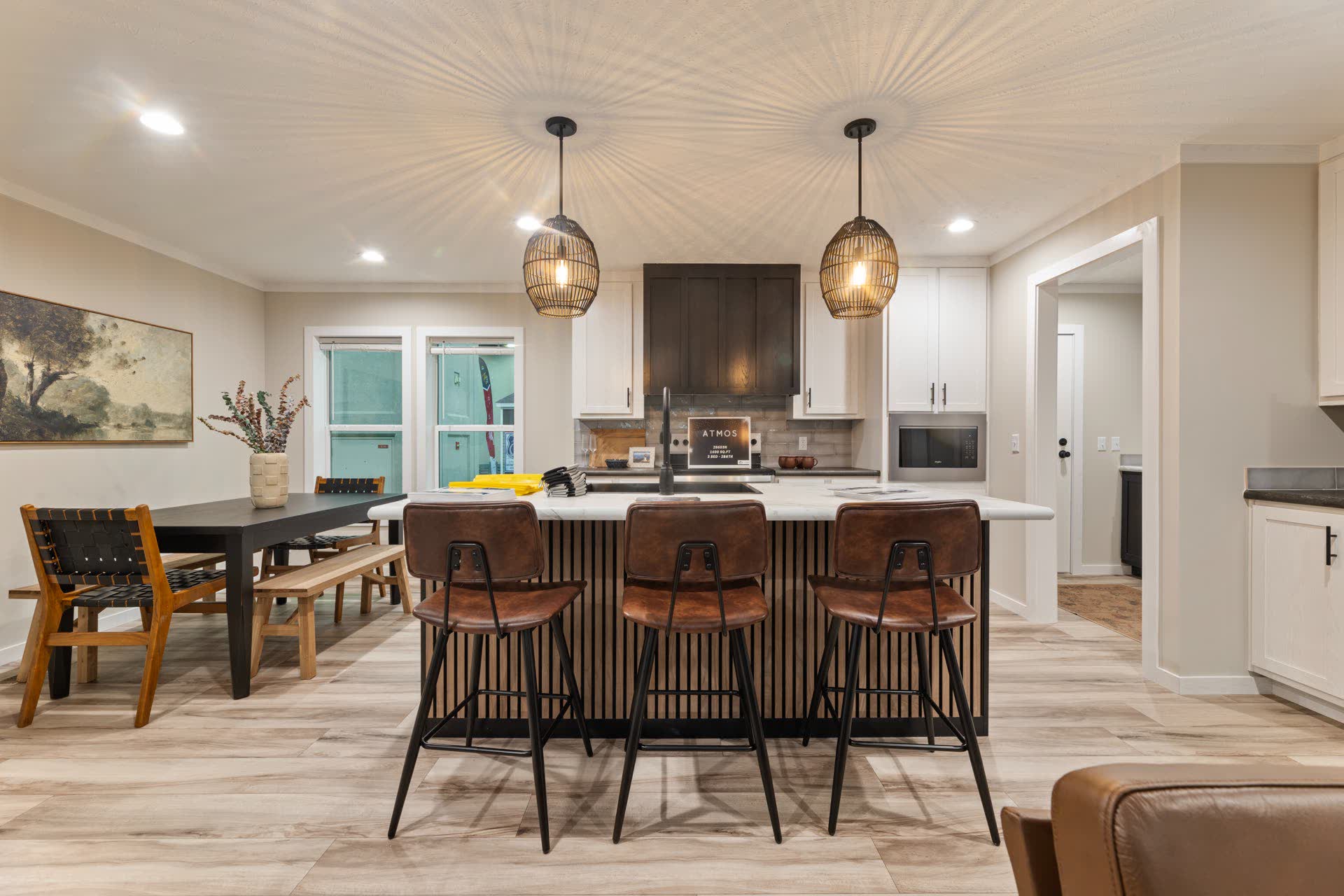 A bright kitchen and dining room with a dark island, leather stools and pendant lights.