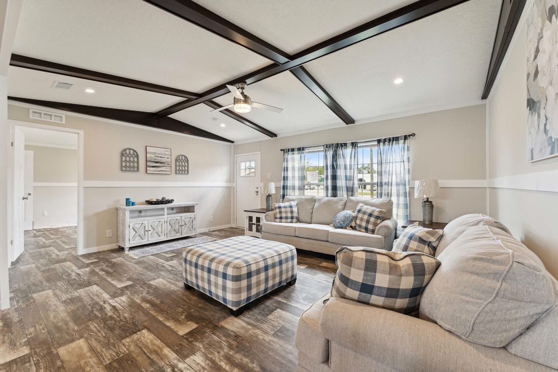 A living room with a vaulted ceiling, dark wood beams and a plaid ottoman.