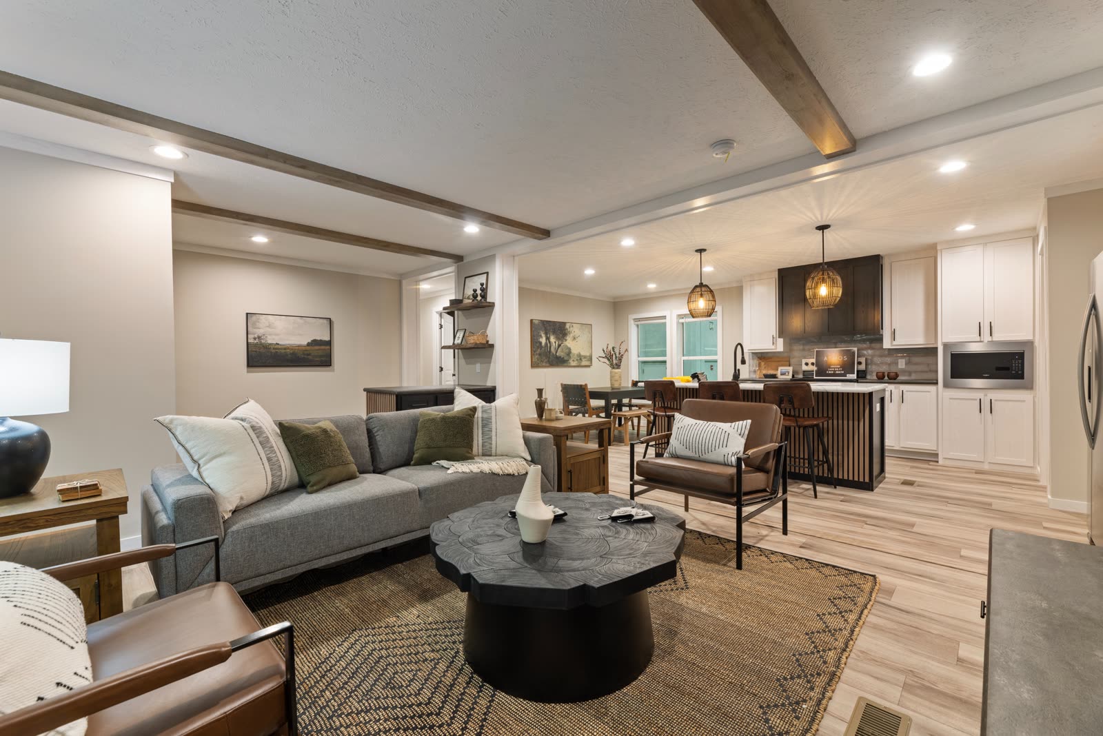 Living room. Grey sofa, leather chairs, round black coffee table, kitchen beyond.