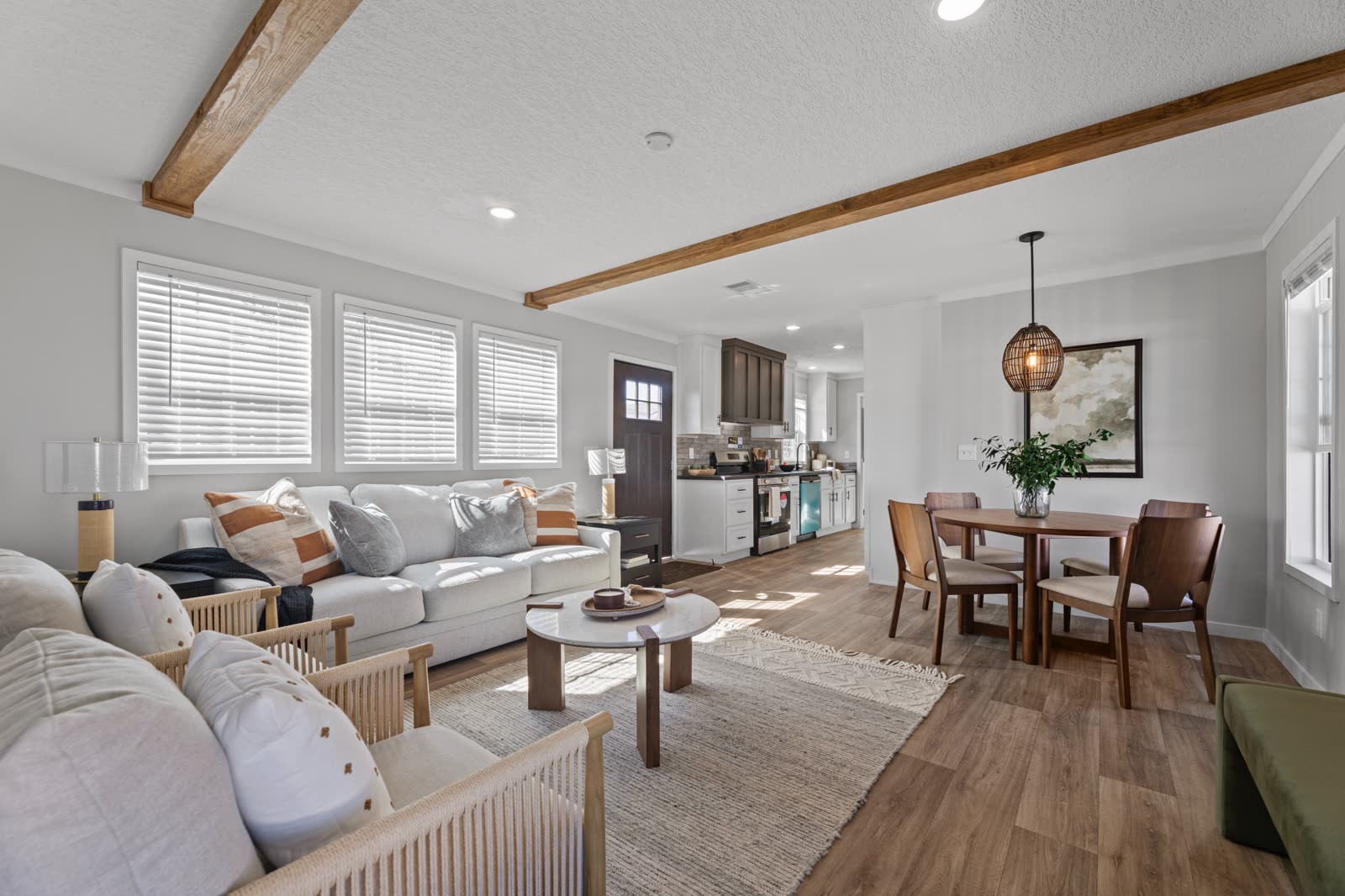 Living and dining. Sectional sofa, round dining table, front door and kitchen beyond. Exposed ceiling beam.