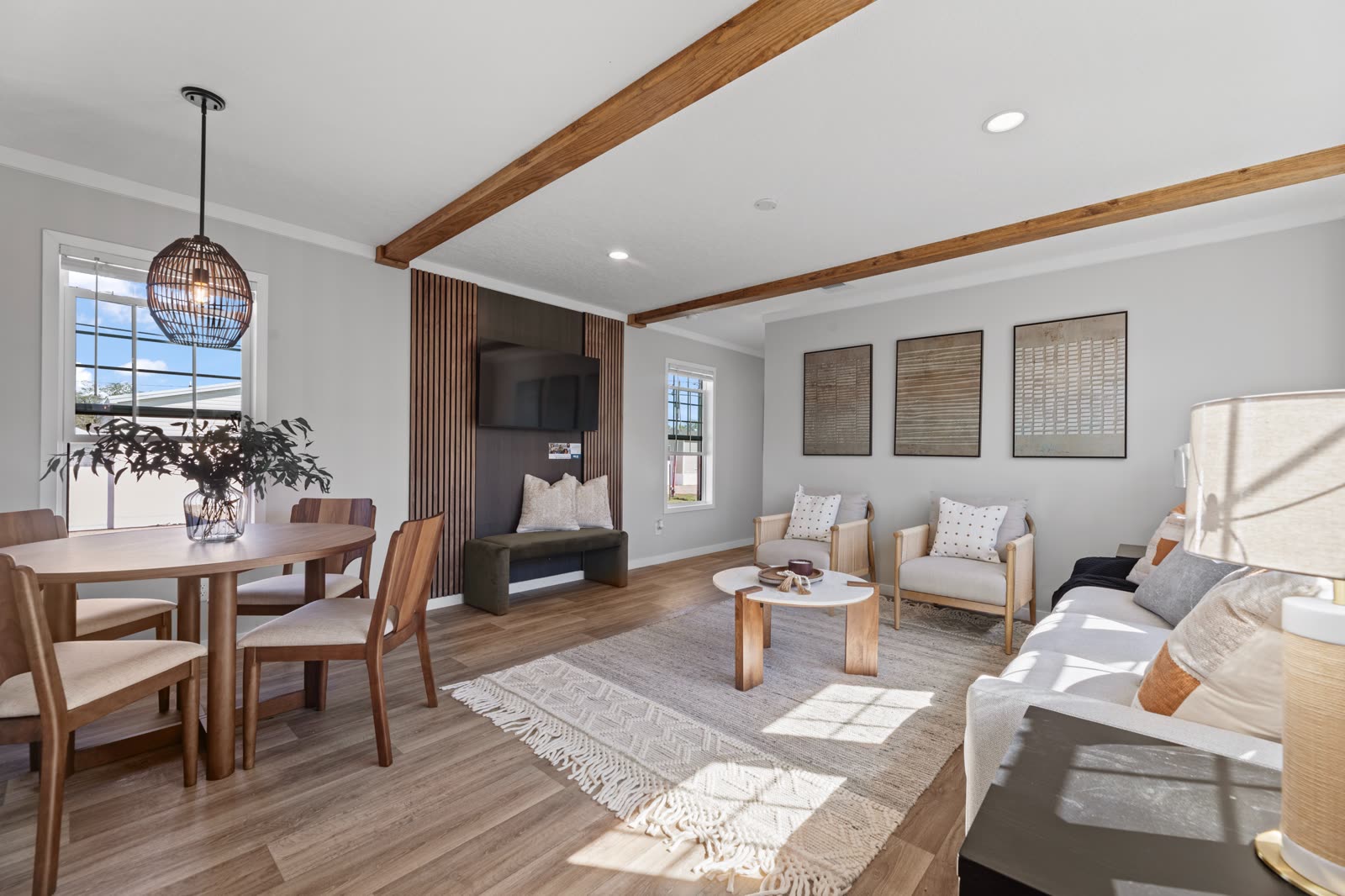 Dining and living. Round wood table, slat accent wall with television, sofa and two armchairs.