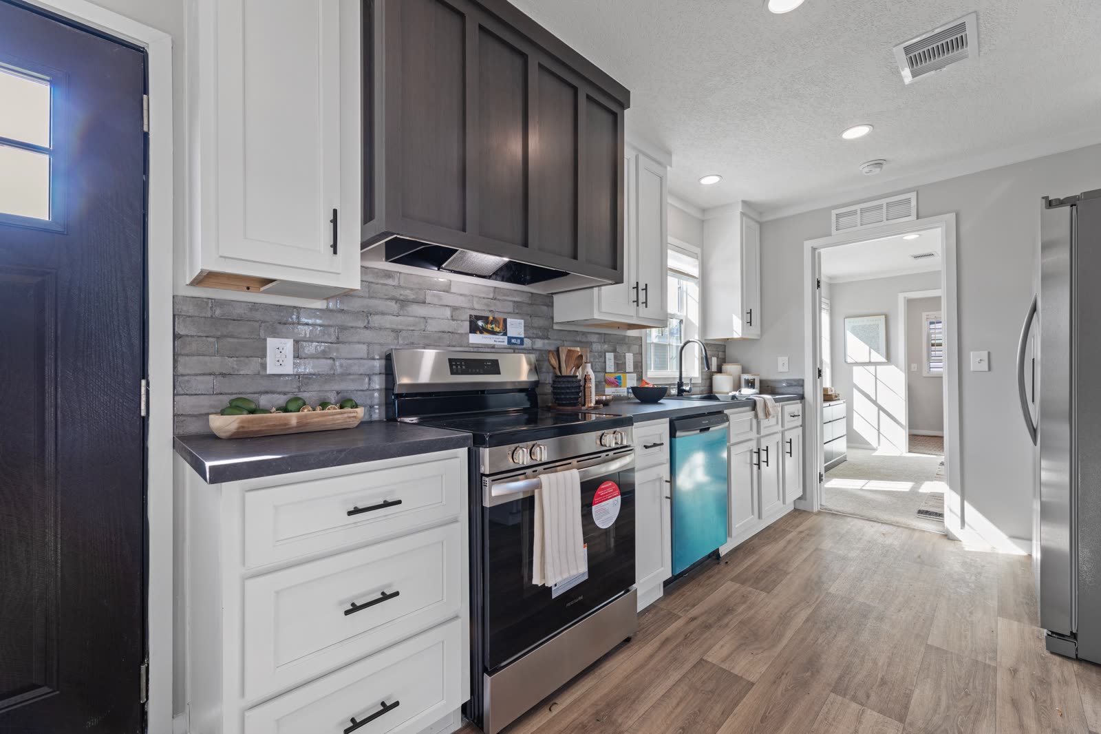 Kitchen. Range with hood, tile backsplash, front door at left, bedroom hall ahead.