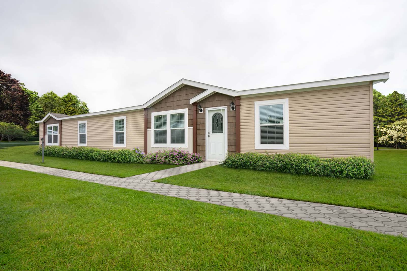 Exterior. Tan vinyl siding, brown gable over the entry, white front door, paver walk.
