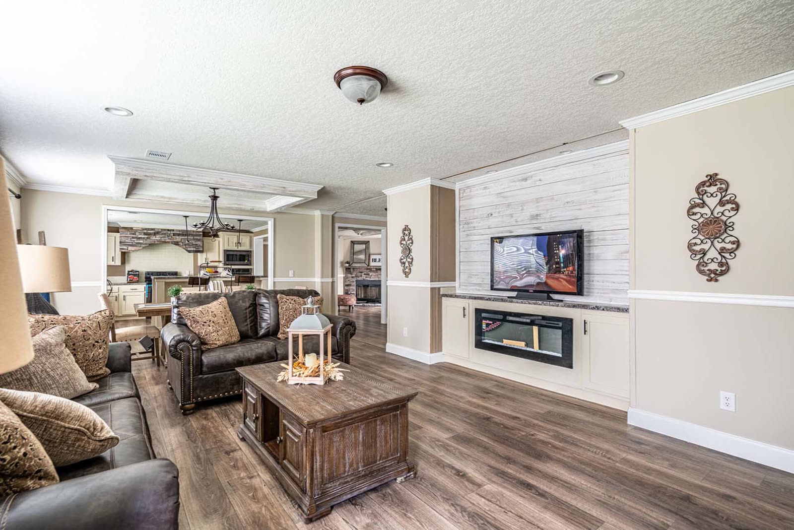 Living room. Leather sofas, wood coffee table, shiplap wall with television and electric fireplace. Dining and kitchen beyond.