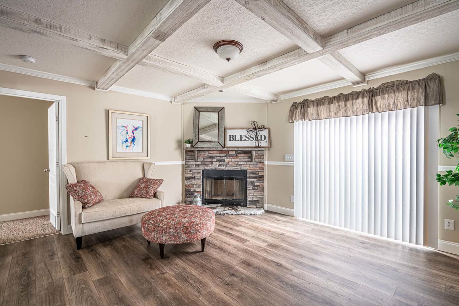 Family room. Coffered ceiling, stone fireplace, armchair and ottoman, sliding glass door with vertical blinds.