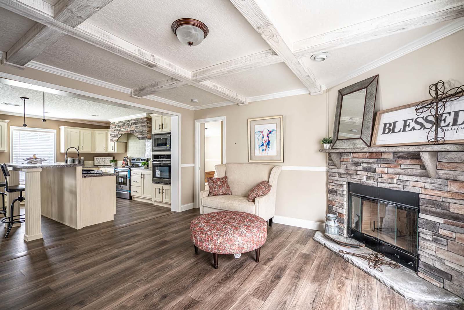 Family room from the kitchen side. Stone fireplace, armchair, kitchen island at left.