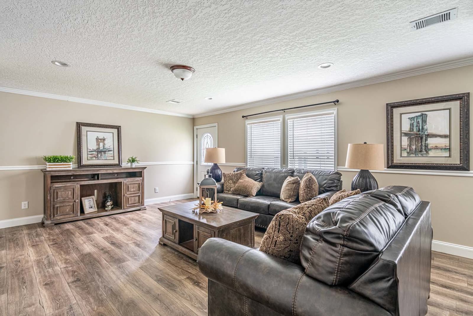Living room. Leather sofa and loveseat, console under the windows, front door at left.