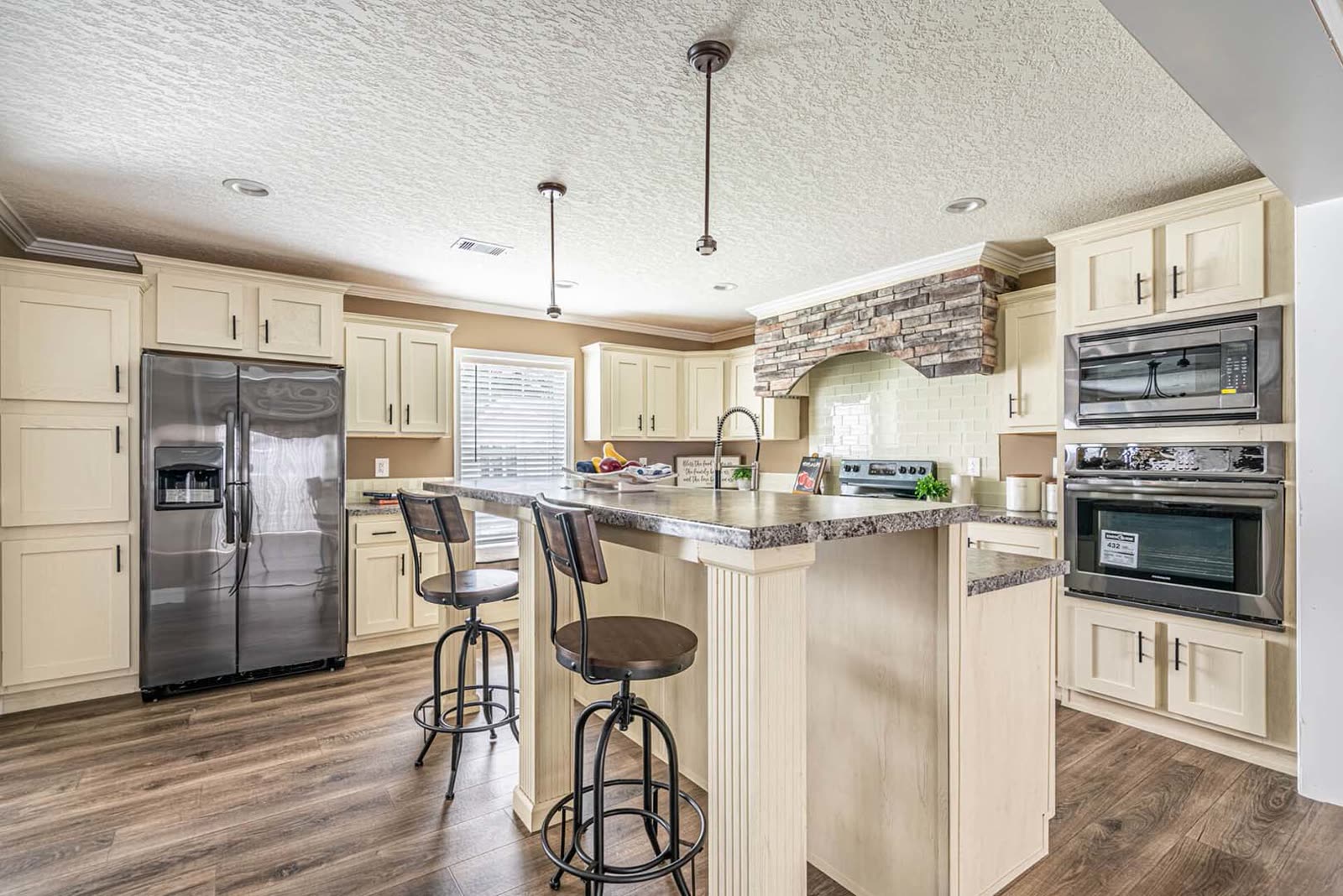 Kitchen. Cream shaker cabinets, island with bar stools, stainless refrigerator, stone range hood surround, wall oven and microwave.