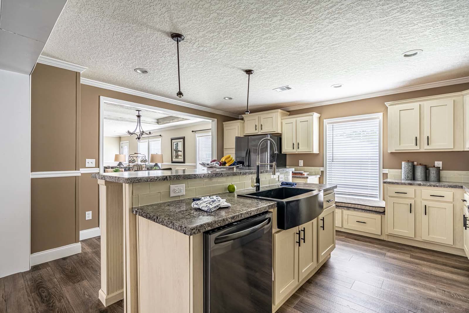 Kitchen island. Grey granite top, black farmhouse sink, dishwasher. Dining room beyond the cased opening.