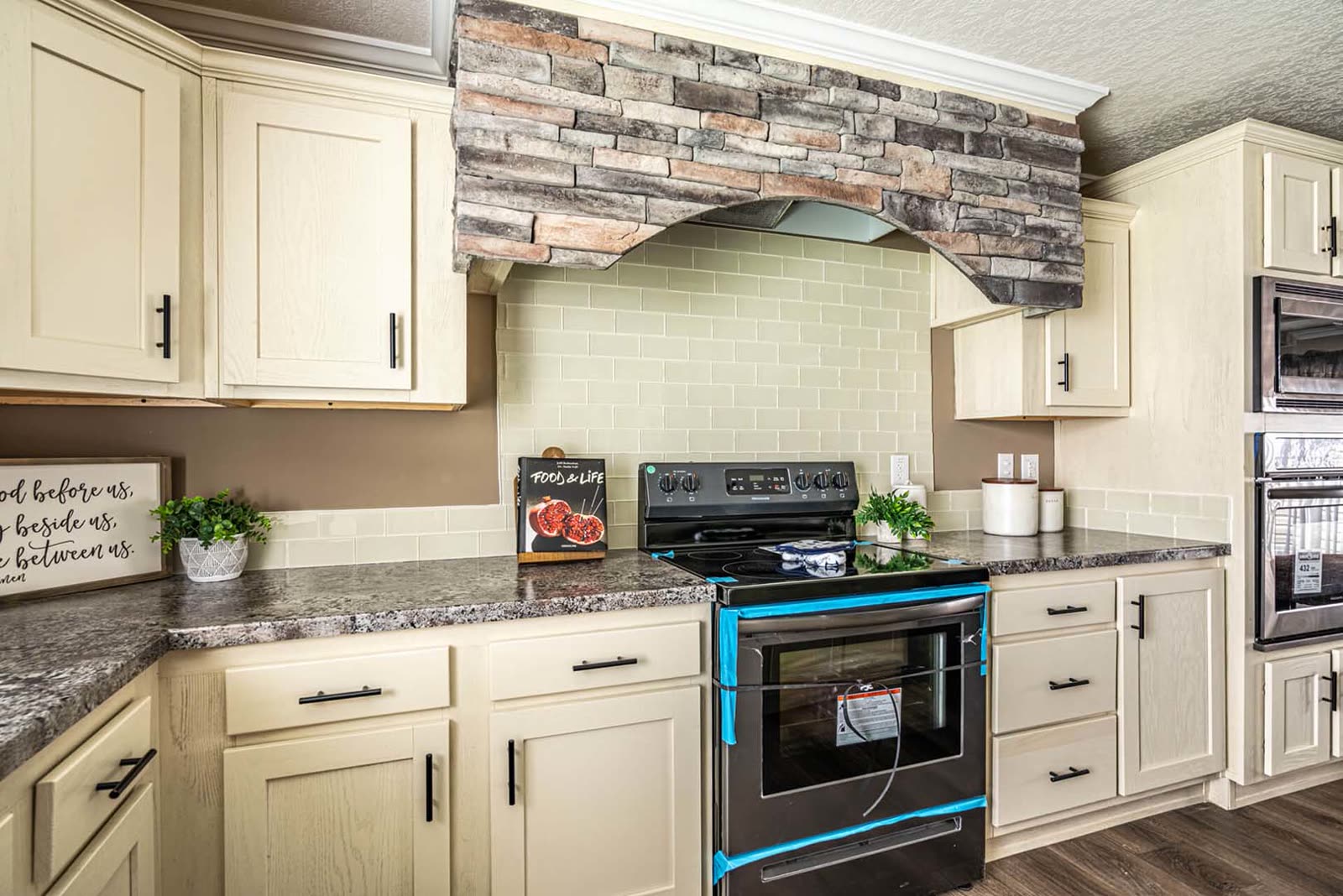 Kitchen. Electric range under the stone hood surround, tile backsplash.