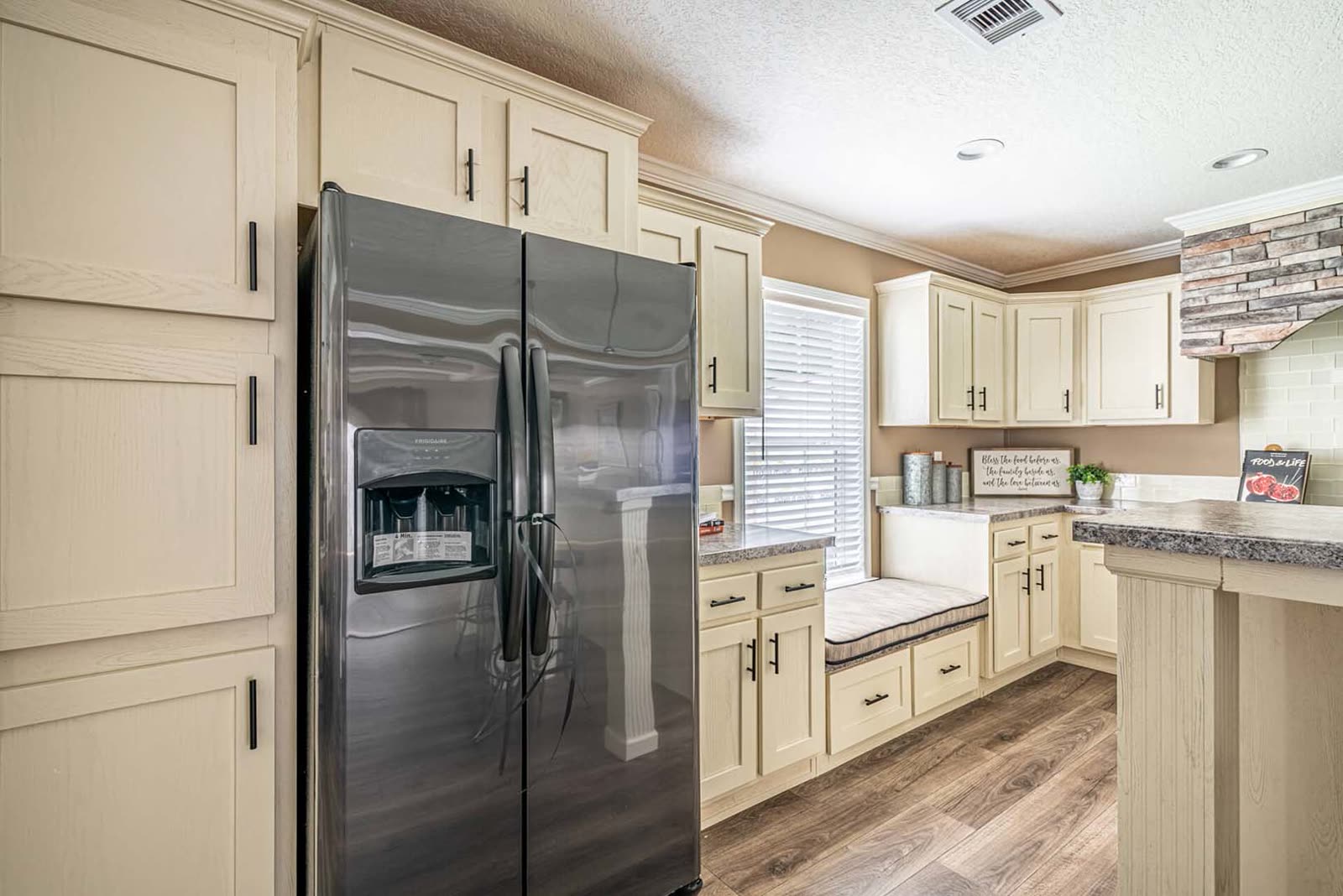 Kitchen. Stainless refrigerator, window seat, island at right.