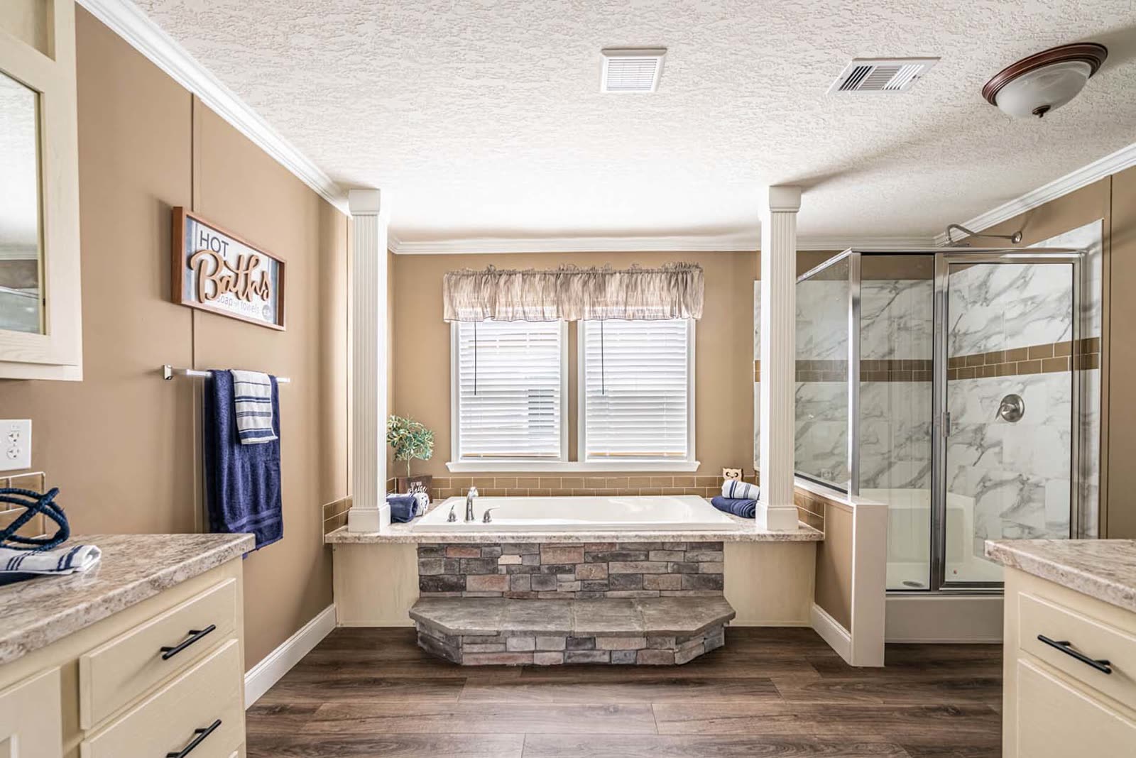 Master bath. Stone-front soaking tub under the window, glass shower at right, vanity at left.
