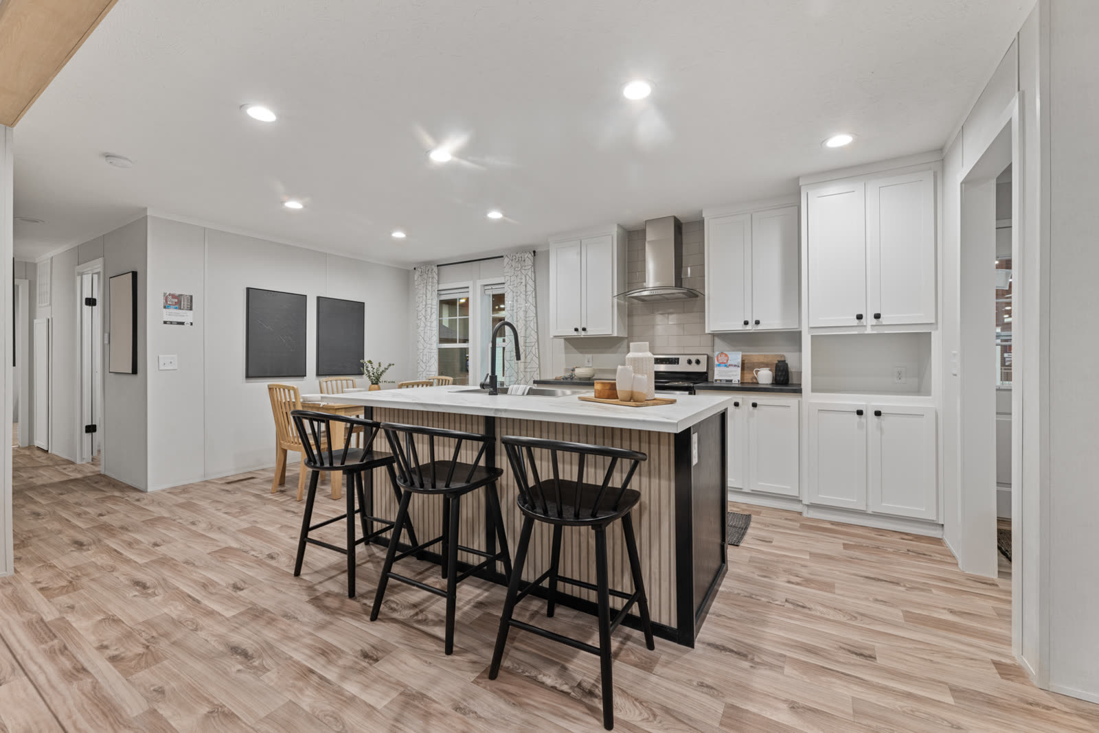 Kitchen island with three black stools. White cabinets, range hood, beadboard island base.