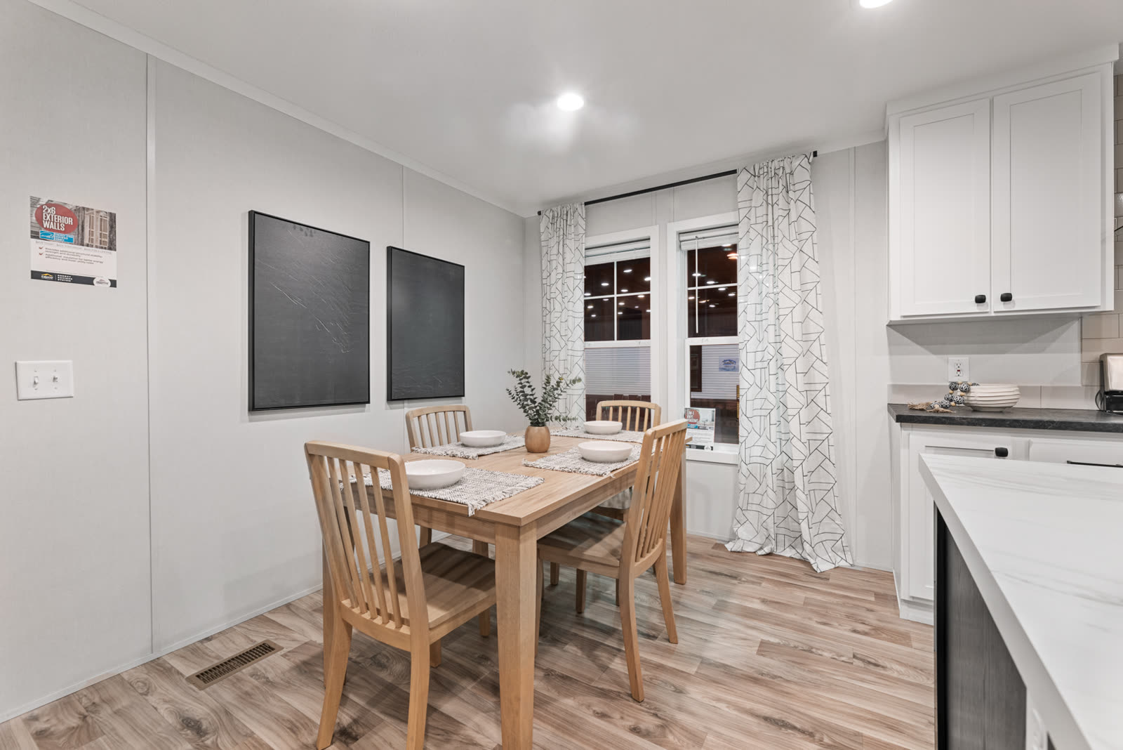 Dining. Table and chairs, curtained windows, two dark panels on the wall.