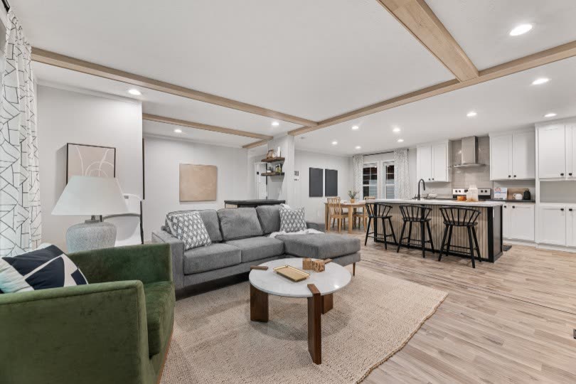 Living room. Grey sectional, green armchair, round coffee table, kitchen beyond.