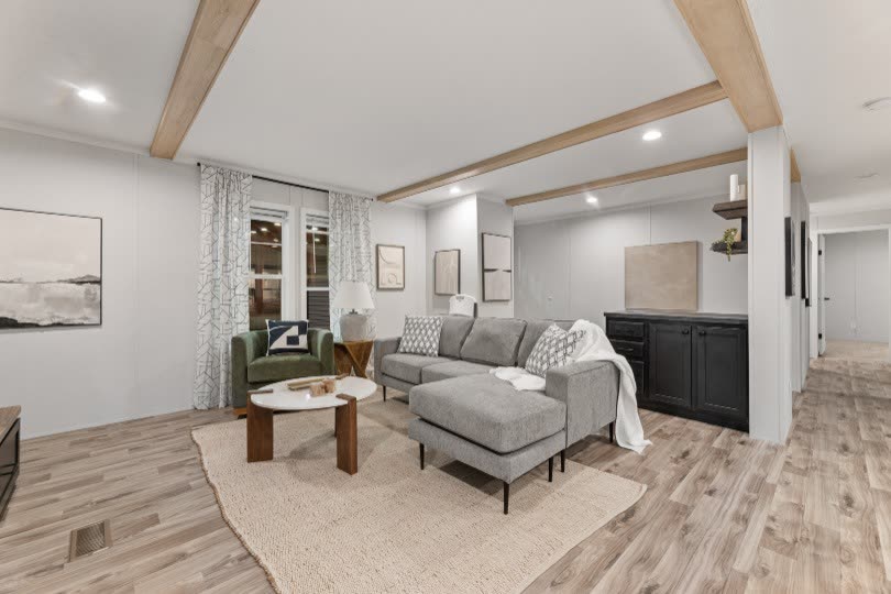Living room. Sectional, green armchair, black cabinet, beamed ceiling.