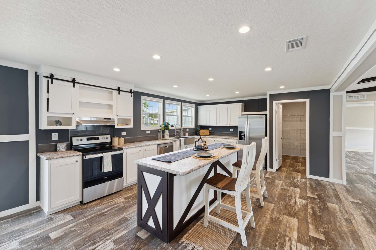 Kitchen, first furnishing. White cabinets, stainless range, island with two stools, utility door beyond.