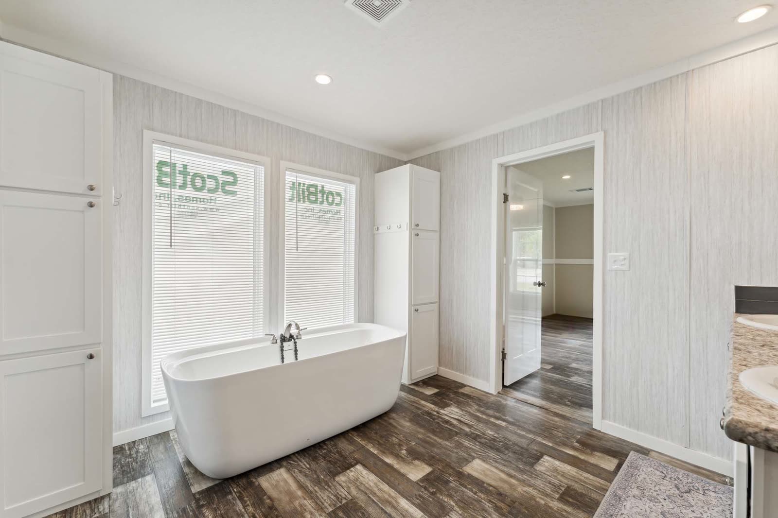 Primary bath. Freestanding tub under the windows, linen cabinet, door to the bedroom.