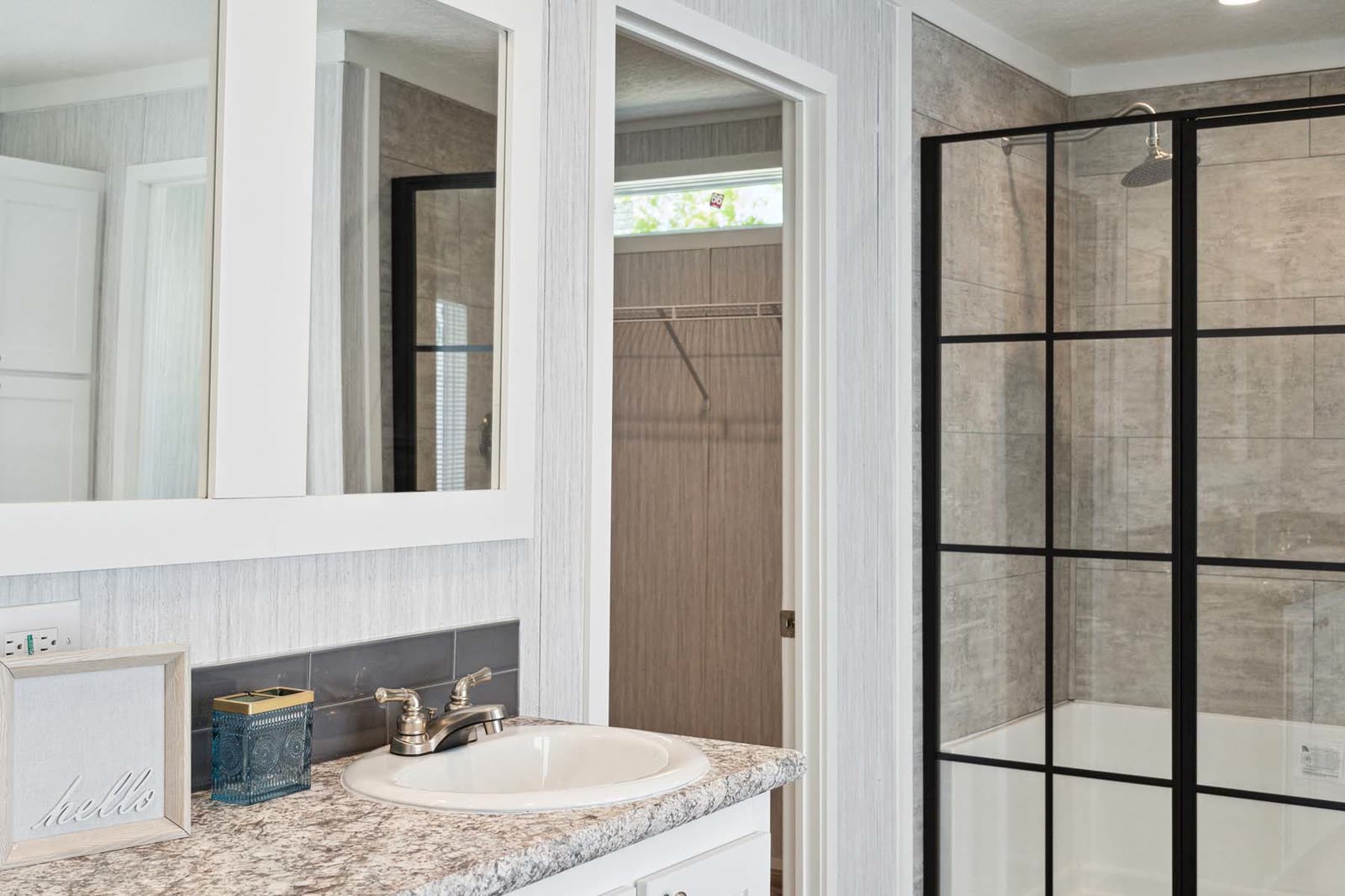 Primary bath. Vanity and mirror, black-framed shower, closet doorway.
