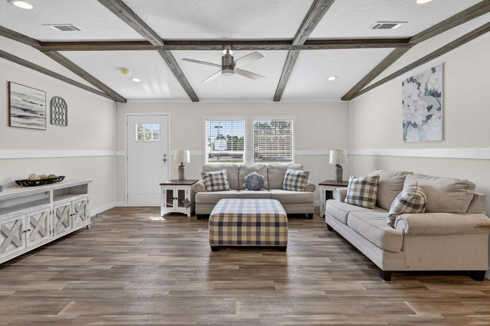 Living room. Sofa and loveseat, plaid ottoman, front door, beamed ceiling.