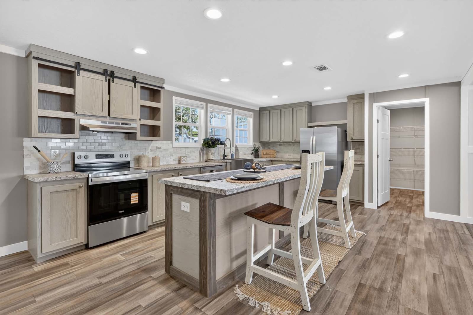 Kitchen. Range wall, island with stools, doorway to the utility room.