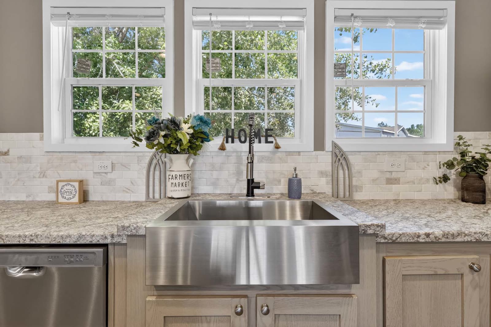 Kitchen. Farmhouse sink under three windows, marble-look backsplash.