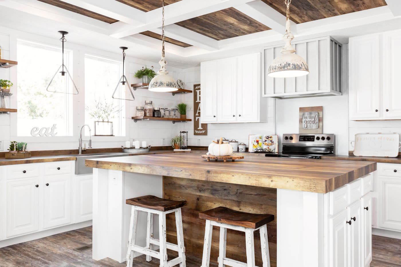 Kitchen. White cabinets, butcher-block island with two stools, coffered beam ceiling, range on the far wall.