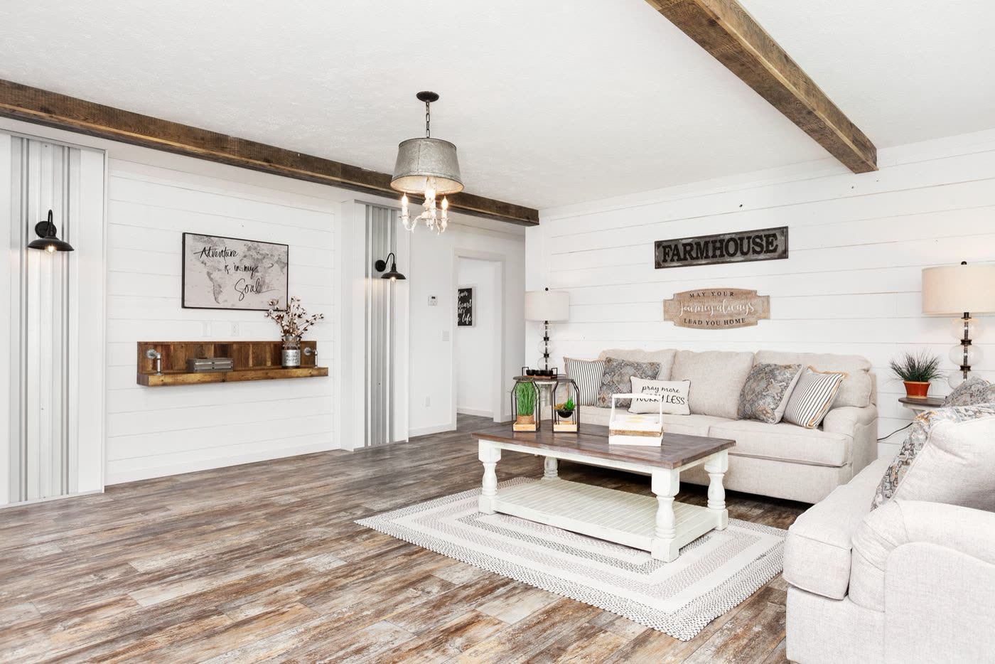 Living room toward the hall. Sofa, coffee table, wood shelf and sconce on the shiplap wall.