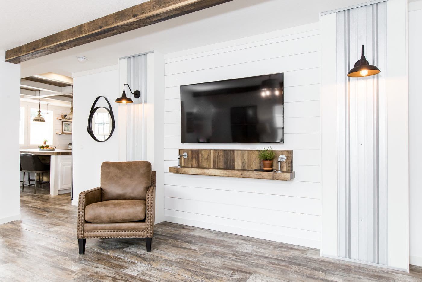Living room, second furnishing. Television on the shiplap wall, leather armchair, kitchen beyond.