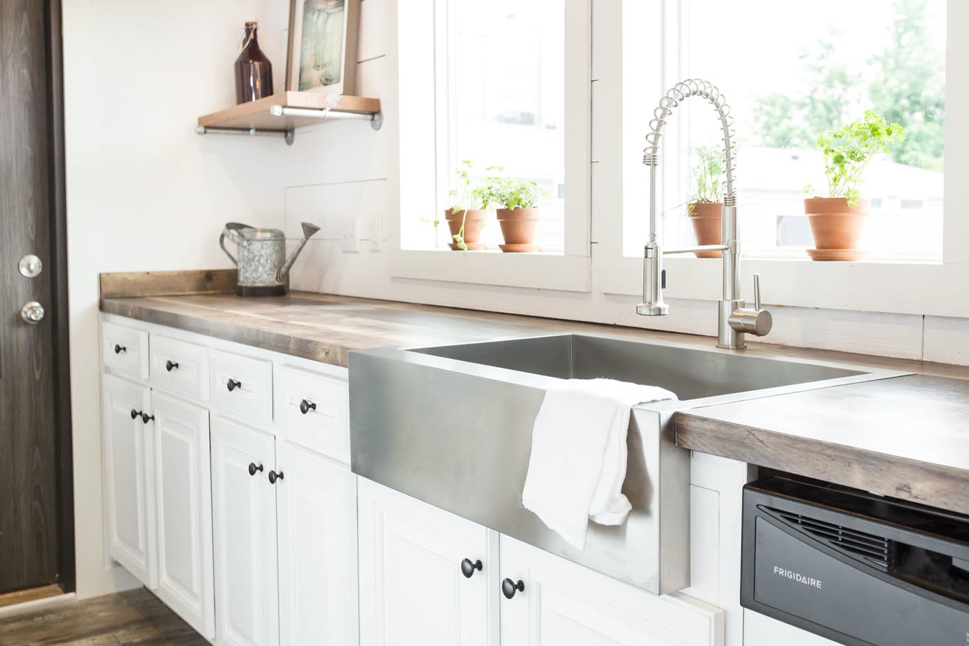 Kitchen. Stainless farmhouse sink, pull-down faucet, dishwasher, potted herbs in the window.