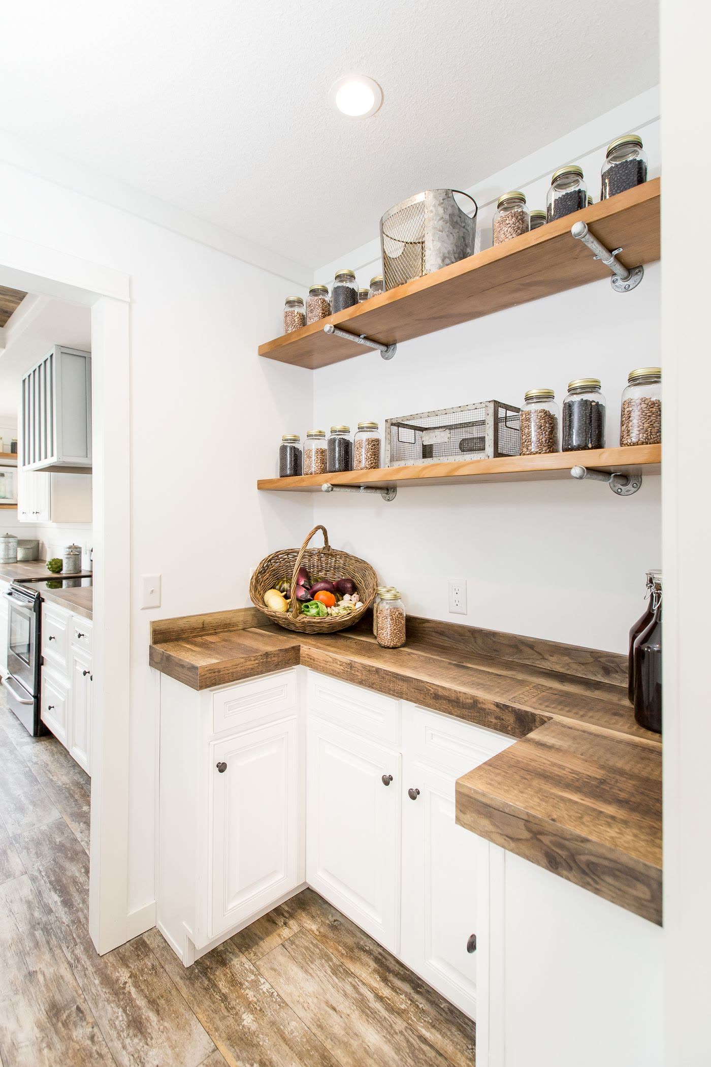 Pantry. Open shelves with jars, L-shaped wood counter, kitchen range to the left.
