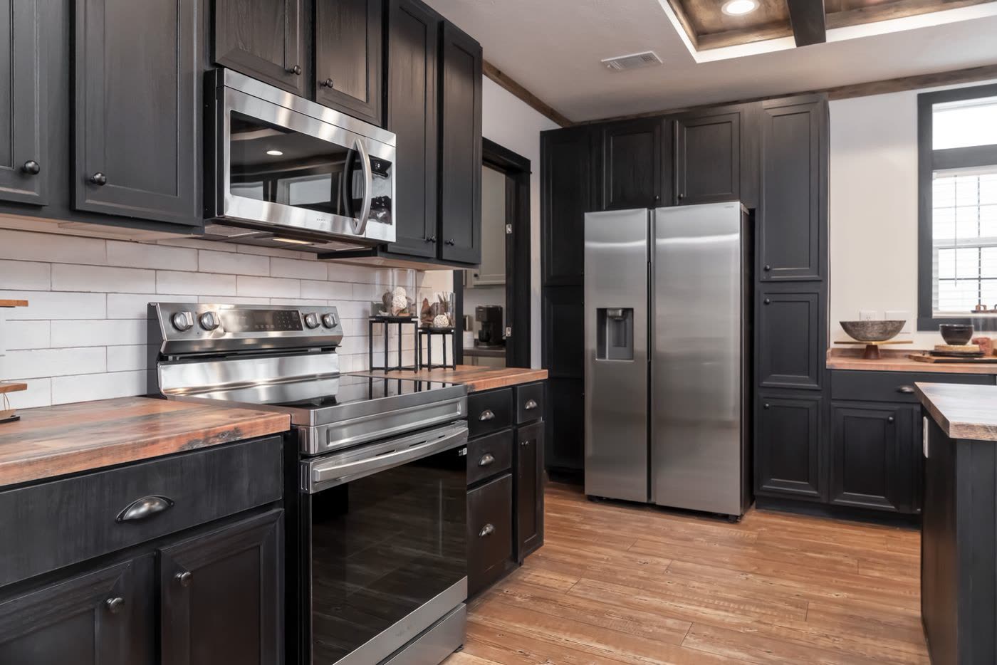 Kitchen. Black cabinets, stainless range and microwave, white subway tile, refrigerator.