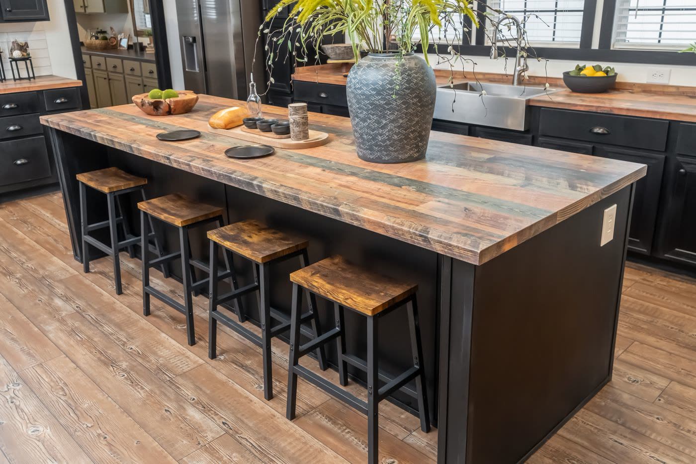 Kitchen island. Wood-look top, four stools, farmhouse sink beyond.
