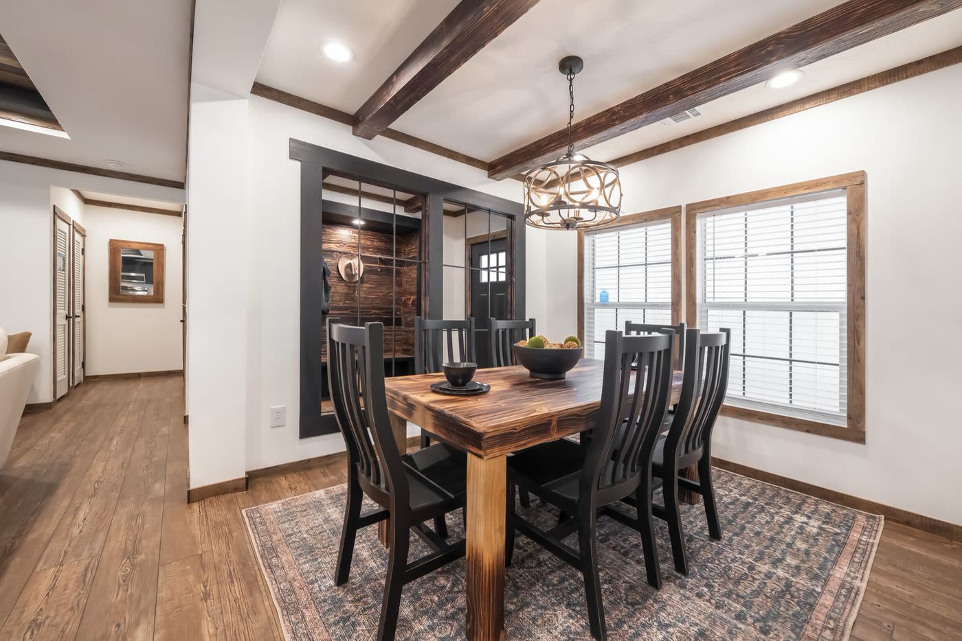 Dining. Wood table with six chairs, patterned rug, chandelier, foyer and front door beyond.