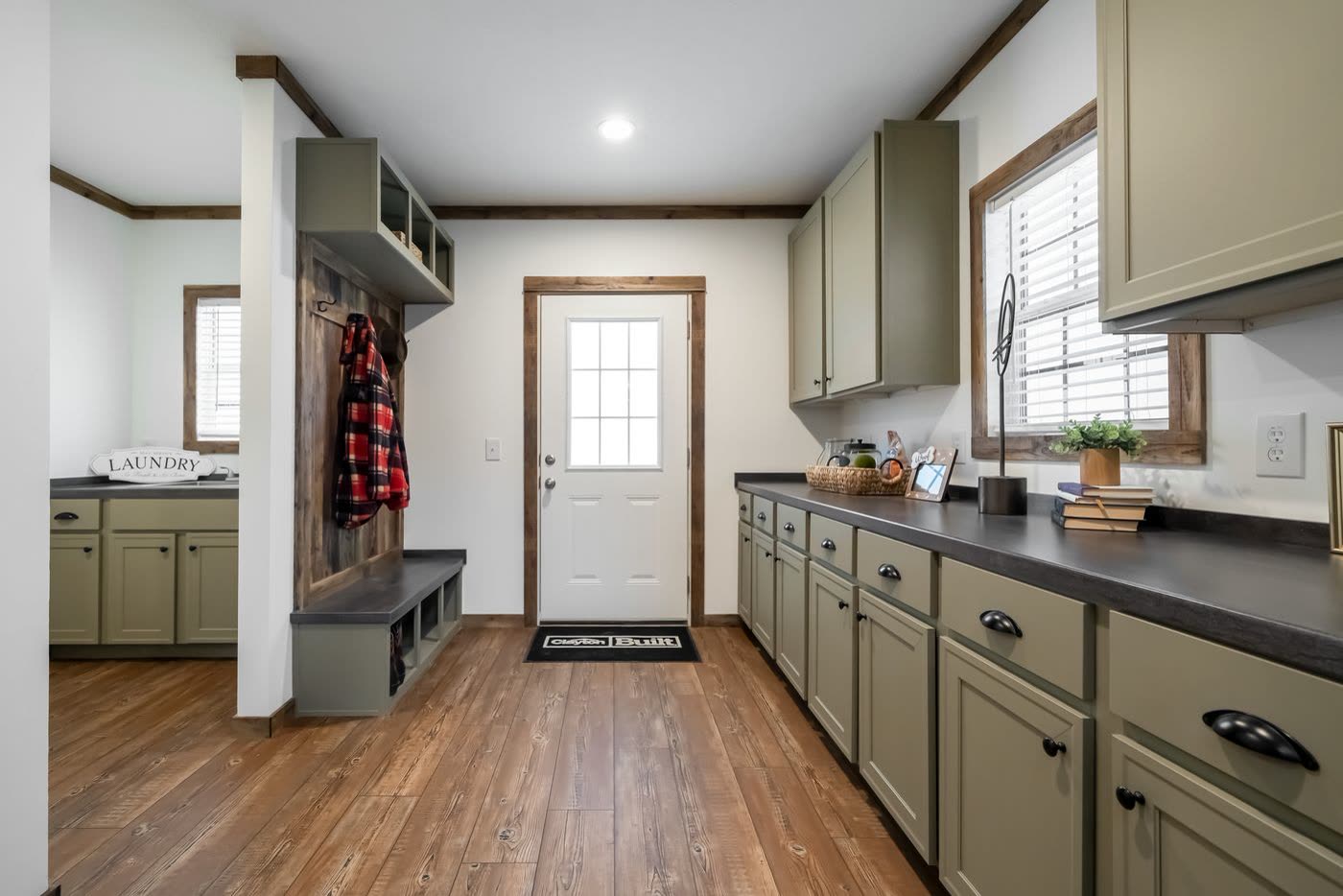 Utility room. Green cabinets, black counter, bench and coat hooks, exterior door.