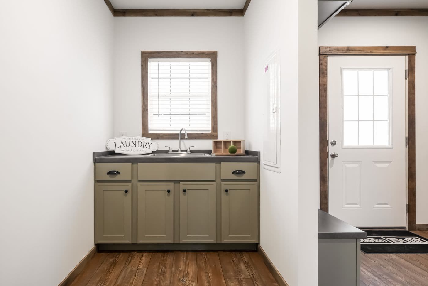 Utility room. Laundry sink and green cabinets under the window, exterior door.