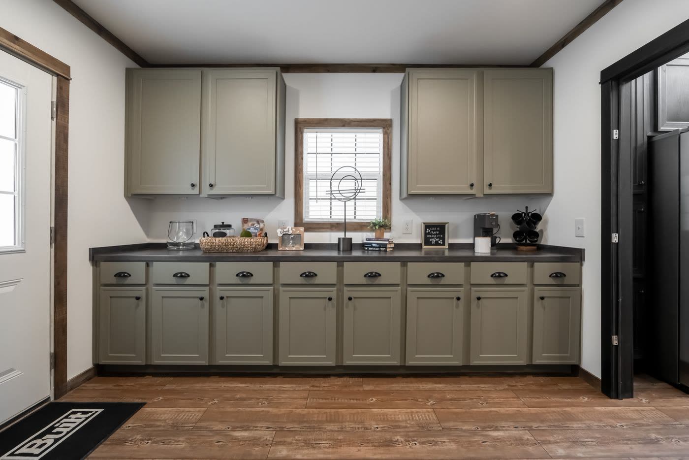 Utility room. Run of green cabinets under the window, doorway to the kitchen at right.