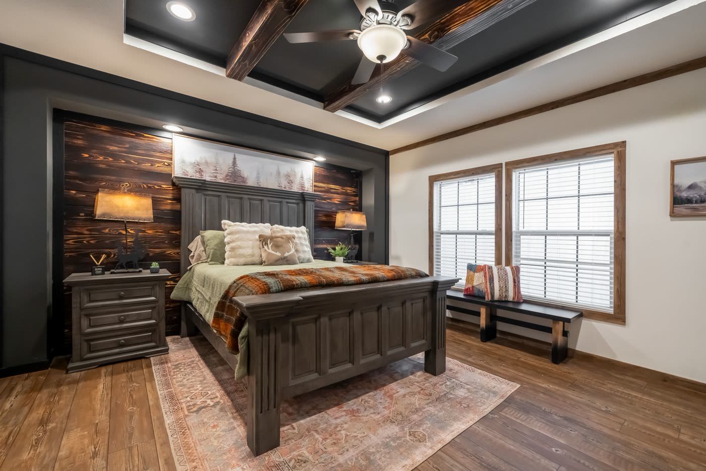 Primary bedroom. Bed against a wood-plank accent wall, tray ceiling with beams, two windows.